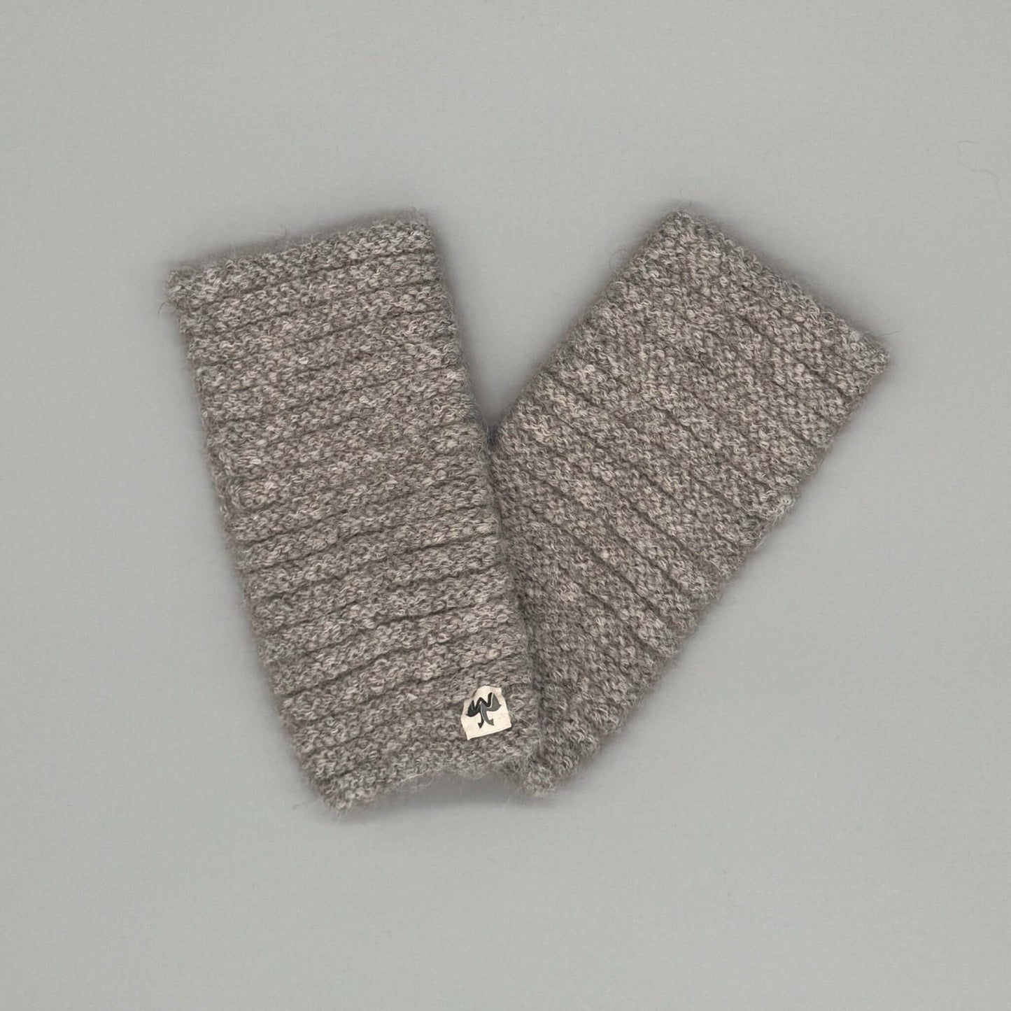 Beige Alpaka Pulswärmer aus Baby-Alpakawolle im Röllchenmuster auf grauem Hintergrund.